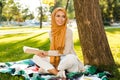 Photo of attractive islamic female student wearing headscarf sitting on blanket in green park