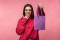 Photo of attractive lady in glasses holds present, surprised and happy. Wears casual pink sweater white pants isolated