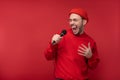 Photo of attractive man with beard in glasses and red clothing. Male sings in microphone karaoke, over red