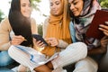 Photo of attractive muslim girls wearing headscarfs sitting on blanket in green park Royalty Free Stock Photo