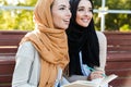 Photo of attractive muslim girls wearing headscarfs sitting in green park