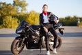 Photo of attractive slim female with ponitail, standing near black fast motobike with helmet in hand, wearing stylish outfit, has