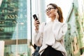 Photo of attractive smiling woman using cellphone and earpod while walking in big city street Royalty Free Stock Photo