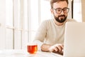 Photo of attractive unshaved man wearing eyeglasses drinking tea