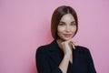 Photo of attractive well groomed businesswoman wears elegant black costume, keeps hand under chin, looks calmly at camera, has