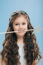 Photo of attractive woman kid with pleasant appearance, has long dark hair, holds magic wand in mouth, poses over blue background Royalty Free Stock Photo