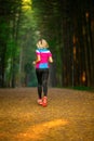 Photo from back of sports woman running through park among trees on summer.