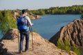 Photo from back of tourist man in cap with walking sticks on mountain hill near lake