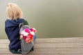 Photo from the back of young blonde dreamy woman with bouquet of flowers in grey backpack near a river. romantic mood Royalty Free Stock Photo