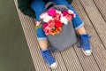 Photo from the back of young blonde dreamy woman with bouquet of flowers in grey backpack near a river. romantic mood Royalty Free Stock Photo