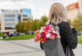 Young blonde romantic woman with bouquet of flowers in grey backpack, standing on a street Royalty Free Stock Photo