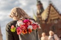 Photo from the back of young blonde romantic woman with bouquet of flowers in grey backpack, standing on a street Royalty Free Stock Photo