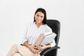 Photo of beautiful brunette businesswoman 30s smiling and holding bunch of paper folders while sitting in black armchair in office Royalty Free Stock Photo