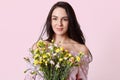 Photo of beautiful brunette young woman with gentle smile, appealing appearance, holds pretty bouquet of spring flowers, rejoices Royalty Free Stock Photo