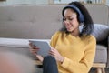 Photo of beautiful dark skin wavy lady homey mood holding digital tablet earflaps listening new audio sitting floor near couch Royalty Free Stock Photo