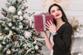 Beautiful girl in a black dress and a dreamy look with a New Year`s gift near the Christmas tree Royalty Free Stock Photo