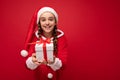 Photo of beautiful happy smiling brunette girl isolated over red background wall wearing santa claus suit holding white Royalty Free Stock Photo