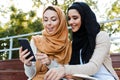 Photo of beautiful muslim girls wearing headscarfs sitting in green park