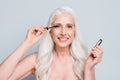 Photo of beautiful retired woman applying brush eyelashes cover extra long flirty lashes isolated grey color background