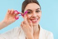 Woman posing over blue background holding lash curler doing makeup