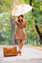 photo of beautiful young woman standing near suitcase with umbrella on the wonderful autumn park background Royalty Free Stock Photo