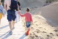 Photo from behind of happy family walking on wooden path on sunny sand beach