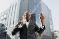 An African American businessman is standing outside with headphones, holding a phone, a video call Royalty Free Stock Photo