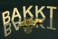 Bitcoin coins in front of bakkt sign made of wood with reflection on the table, Slovenia - December 27th