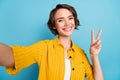 Photo of blogger lady take selfie show v-sign toothy smile wear yellow shirt isolated blue color background