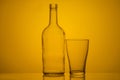 Photo of a bottle and glass with back lighting on a yellow background