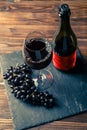 Photo of bottle of red wine, wine glass with wine, black grapes on stone board Royalty Free Stock Photo