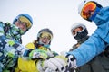 Photo from bottom of four happy snowboarders in helmet doing handshake on blue sky.