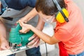 Photo of a boy in protective glasses and headphones tinkering using jig saw in wood workshop