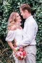 Bride and groom with a bouquet of peonies posing against the backdrop of the forest Royalty Free Stock Photo