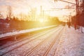 Photo of bright and beautiful sunset on a cloudy sky in cold winter season. Railway track with platforms for waiting trains and p