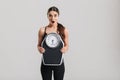 Photo of brunette athletic woman holding scale and expressing surprise on face, isolated over gray background