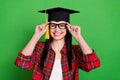 Photo of brunette funny young lady touch spectacles wear graduation cap shirt isolated on green color background