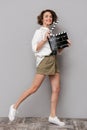 Photo of brunette woman 20s smiling and holding black clapperboard, isolated over gray background