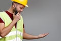 Photo of builder in helmet with walkie-talkie in his hand in yellow vest with raised palm up. Royalty Free Stock Photo