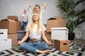 Photo of calm blonde sitting on floor among cardboard boxes and boy, girl jumping on sofa Royalty Free Stock Photo