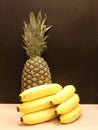 Still life with a pineapple standing behind bananas lying on a wooden table against a black wall. Royalty Free Stock Photo