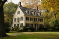 A photo capturing a grand white house nestled amidst a vibrant autumn forest with an array of colorful trees, Early American Royalty Free Stock Photo