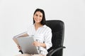 Photo of caucasian brunette businesswoman 30s smiling and holding bunch of paper folders while sitting in black armchair in office Royalty Free Stock Photo