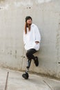 Photo of caucasian disabled girl with bionic leg in casual wear, standing and smiling outdoor over concrete wall