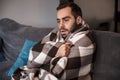 Photo of caucasian man 30s wrapped in blanket having temperature and looking sick on sofa in apartment