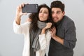 Photo of caucasian man and woman taking selfie photo on smartphone, isolated over gray background Royalty Free Stock Photo