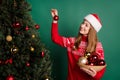 Photo of celbrate young lady put toys on tree wear new year sweater cap  on green color background Royalty Free Stock Photo