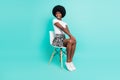 Photo of charming cute dark skin woman dressed casual outfit sitting chair smiling isolated turquoise color background Royalty Free Stock Photo