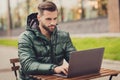 Photo of charming cute young guy dressed green coat having rest sitting cafeteria writing modern gadget outdoors city