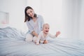 Photo of charming funny small baby mom wear blue shirt holding crawling bed smiling indoors home room Royalty Free Stock Photo